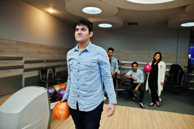 Hombre del sur de Asia en camisa de jeans de pie en la bolera con la pelota en las manos Guy se está preparando para un lanzamiento