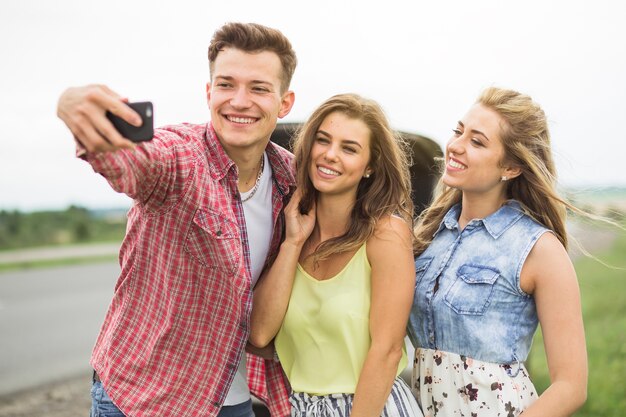 Hombre con sus dos amigas tomando autorretrato en el teléfono celular