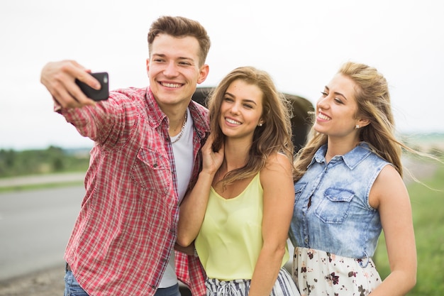 Hombre con sus dos amigas tomando autorretrato en el teléfono celular