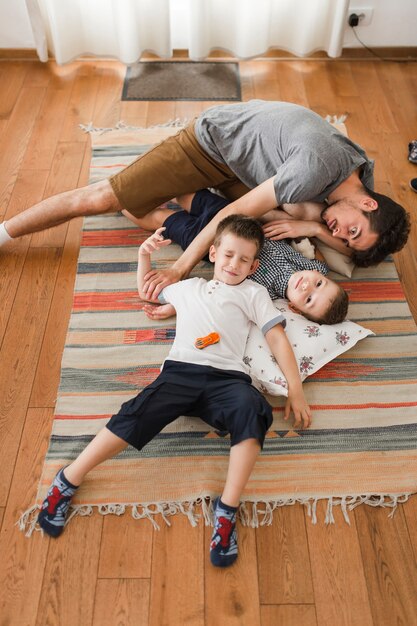 Hombre y sus dos hijos descansando en una alfombra.