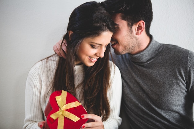 Hombre susurrando algo a su novia mientras ella sujeta un regalo