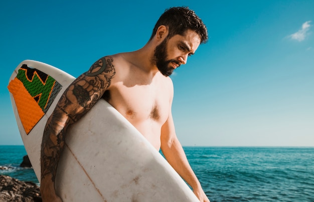 Foto gratuita hombre con tabla de surf caminando cerca del mar