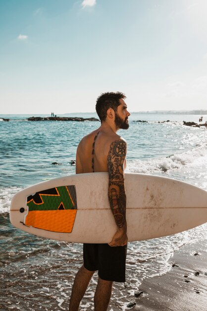 Hombre con tabla de surf caminando en la orilla arenosa