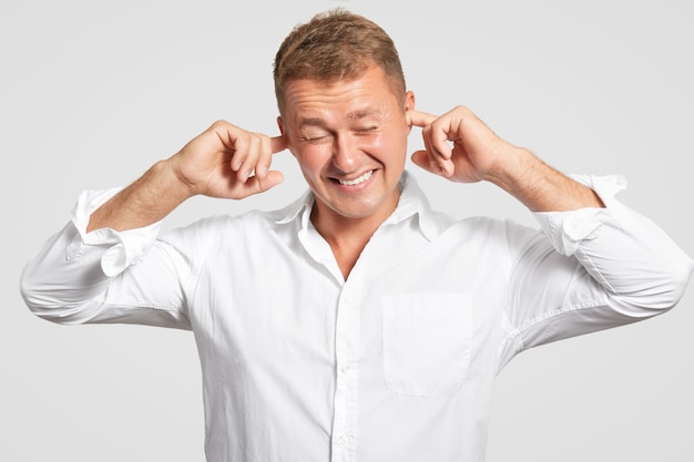 El hombre se tapa los oídos, aprieta los dientes, ignora el sonido fuerte, se viste con una elegante camisa blanca, no quiere escuchar