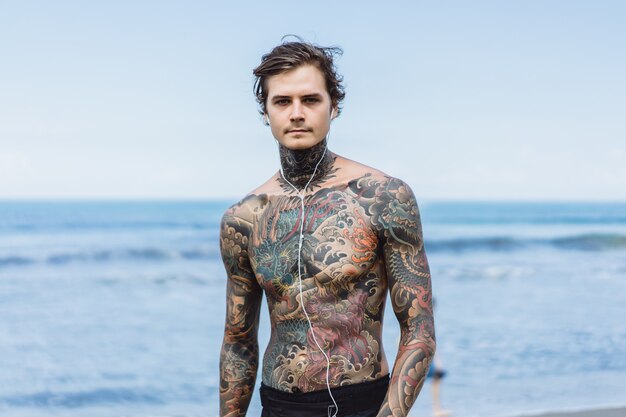 hombre tatuado con auriculares contra el cielo azul en el océano