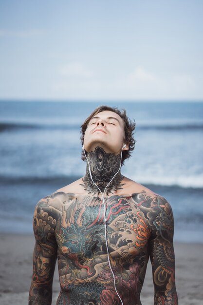 hombre tatuado con auriculares contra el cielo azul en el océano