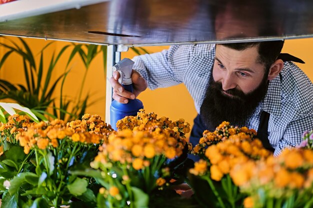 Foto gratuita hombre tatuado con barba regando flores en una tienda de mercado.