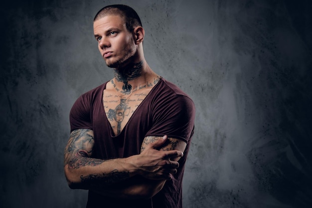 Hombre tatuado con brazos cruzados sobre fondo artístico gris.
