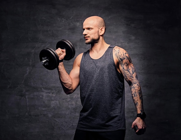 Hombre tatuado con la cabeza rapada atlética haciendo ejercicios de bíceps con pesas.