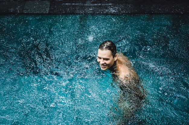 hombre tatuado en la piscina bajo la lluvia.