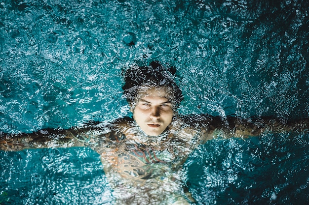 hombre tatuado en la piscina bajo la lluvia.