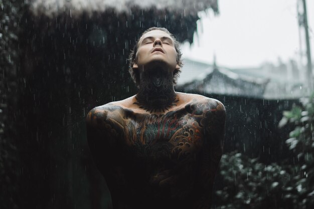 Hombre tatuado posando bajo la lluvia