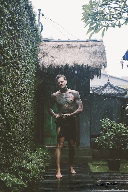 Foto gratuita hombre tatuado posando bajo la lluvia