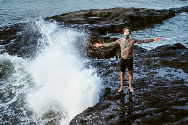 Un hombre tatuado yace al borde de un acantilado. salpicaduras de las olas del océano.