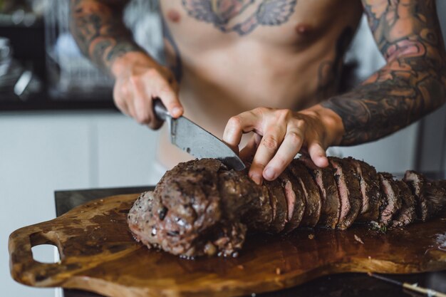 Hombre en tatuajes corta carne.