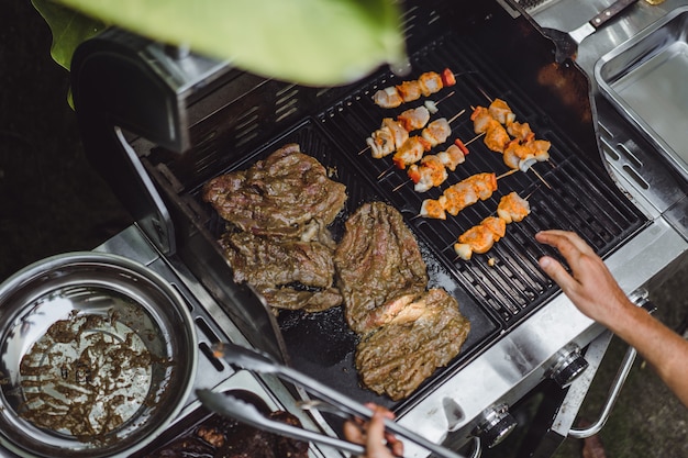 Un hombre en tatuajes hace barbacoa parrilla carne al aire libre.