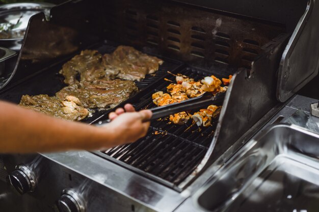 Un hombre en tatuajes hace barbacoa parrilla carne al aire libre.