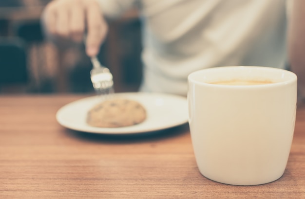 Un hombre con la taza de café y la galleta en color de la vendimia de la cafetería