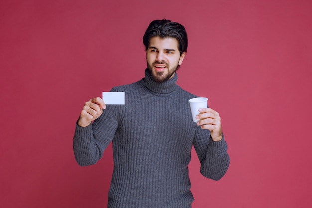 Hombre con una taza de café mostrando su factura o tarjeta de visita.