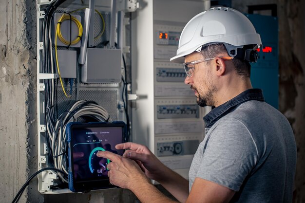 El hombre, un técnico eléctrico que trabaja en un cuadro de distribución con fusibles, usa una tableta