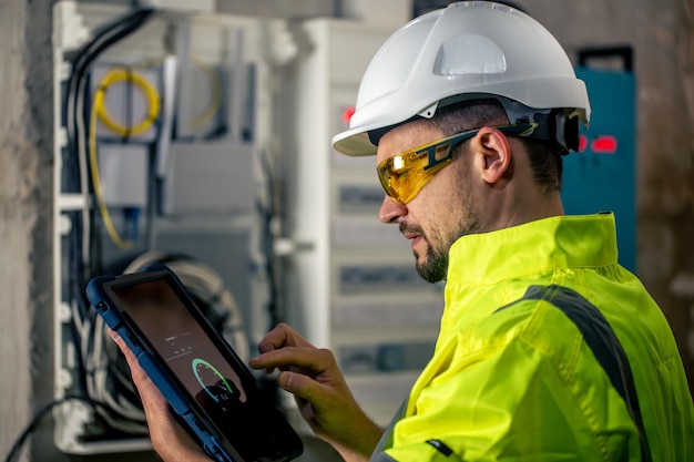 El hombre, un técnico eléctrico que trabaja en un cuadro de distribución con fusibles, usa una tableta