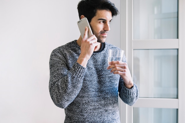 Hombre con teléfono inteligente y agua cerca de la ventana