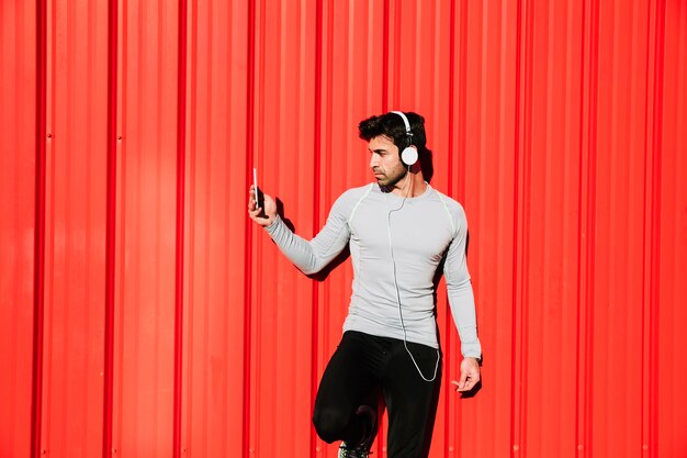 Hombre con teléfono inteligente y auriculares cerca de la pared