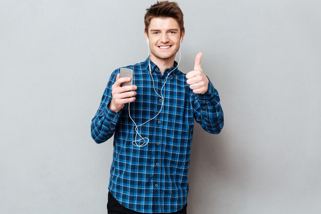 Hombre con teléfono inteligente y auriculares mostrando los pulgares para arriba