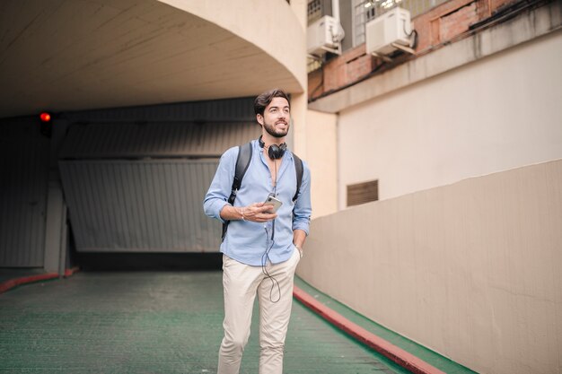 Hombre con teléfono inteligente caminando cerca del edificio