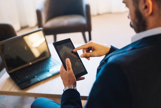 Hombre con teléfono inteligente en la computadora portátil