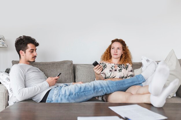 Hombre con teléfono inteligente sentado cerca de su esposa viendo la televisión