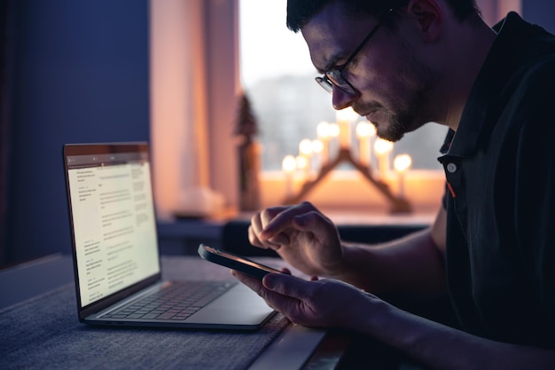 Foto gratuita un hombre con un teléfono inteligente se sienta frente a una computadora portátil a altas horas de la noche