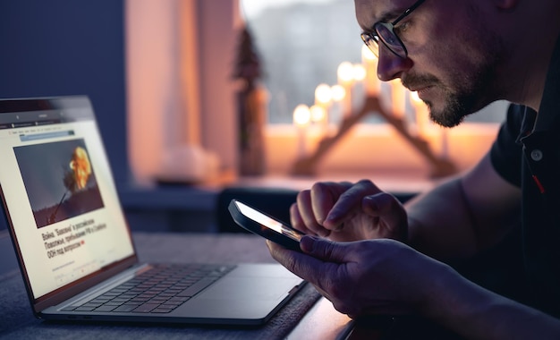 Foto gratuita un hombre con un teléfono inteligente se sienta frente a una computadora portátil a altas horas de la noche