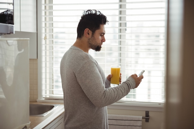 Hombre con teléfono móvil mientras toma jugo en la cocina