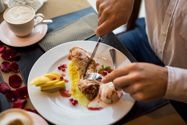 Hombre con tenedor y cuchillo cortando delicioso postre fresco en restaurante