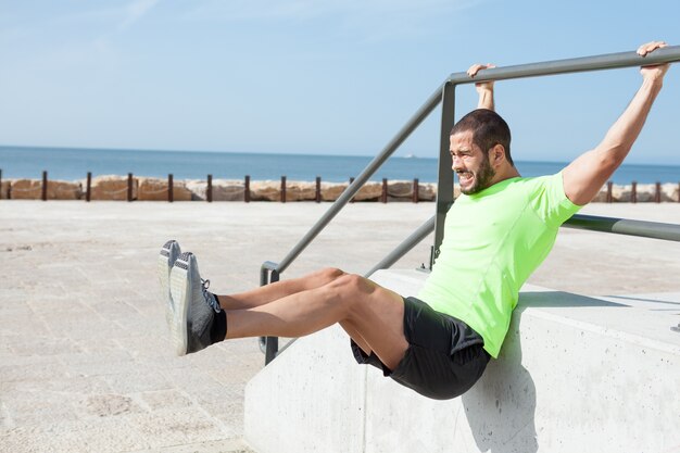 Hombre tenso haciendo suspensión de piernas en el mar