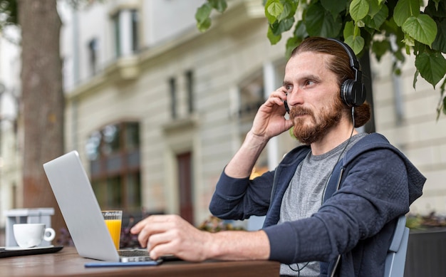 Hombre en una terraza de la ciudad trabajando en la computadora portátil mientras usa auriculares