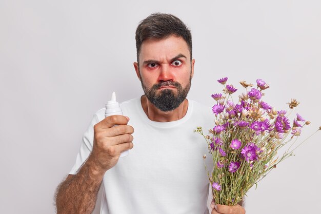 El hombre tiene aerosol para curar la reacción alérgica tiene alergia a las flores silvestres sufre de rinitis y los ojos llorosos posa en blanco