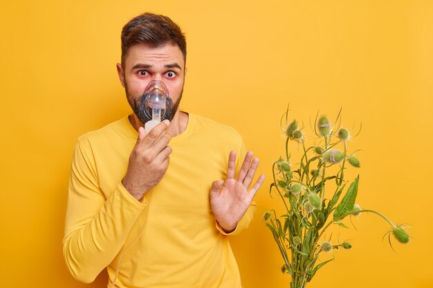 el hombre tiene problemas con los pulmones sufre de asma síntomas de alergia tiene ojos rojos hinchazón se mantiene alejado del alérgeno es alérgico al polen usa una máscara de inhalación aislada en una pared amarilla