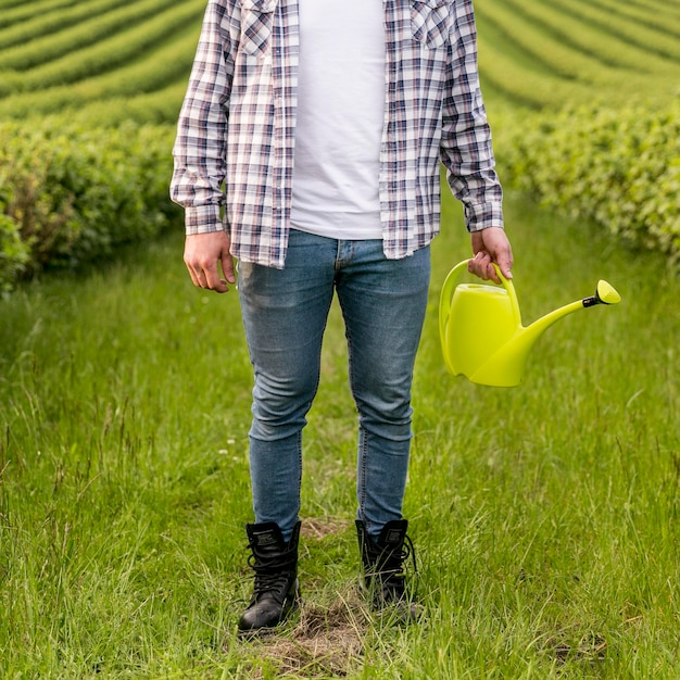 Hombre en tierras de cultivo con primer plano de regadera