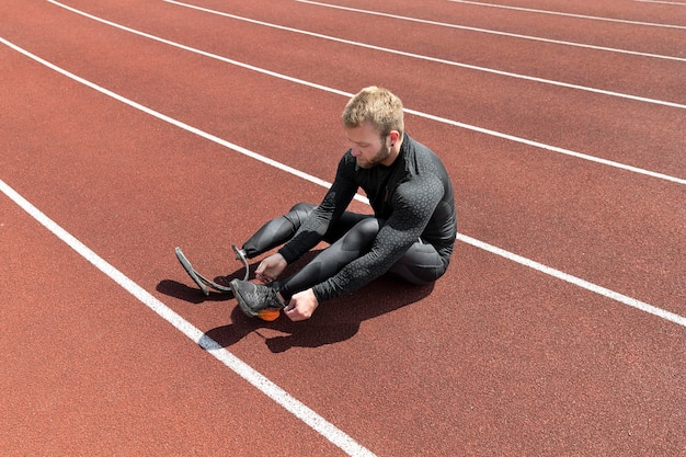 Hombre de tiro completo atando los cordones de los zapatos en la pista de atletismo