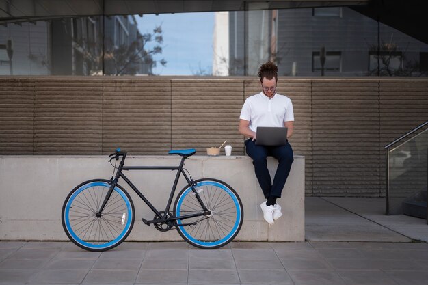 Hombre de tiro completo con computadora portátil y bicicleta al aire libre