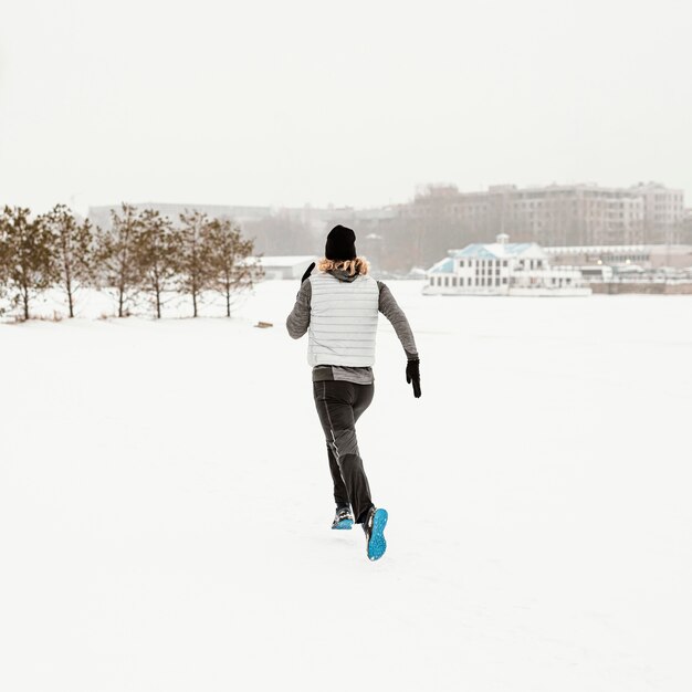 Hombre de tiro completo corriendo en la nieve