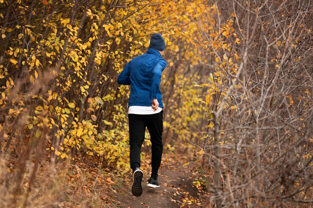 Hombre de tiro completo corriendo en sendero en el bosque