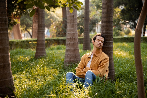 Foto gratuita hombre de tiro completo durmiendo cerca del árbol