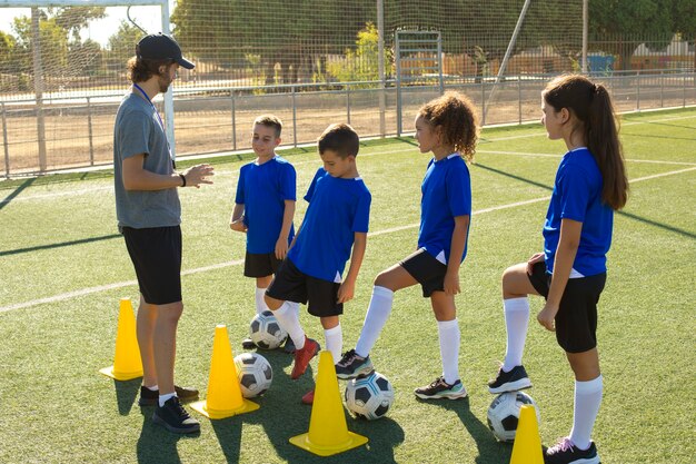 Hombre de tiro completo entrenando a niños jugando al fútbol