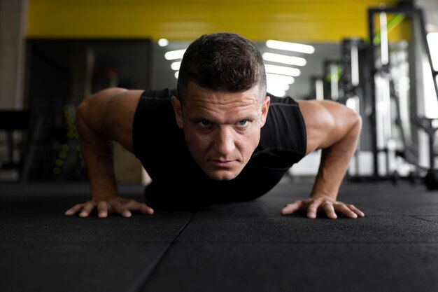 Hombre de tiro completo haciendo flexiones en el gimnasio