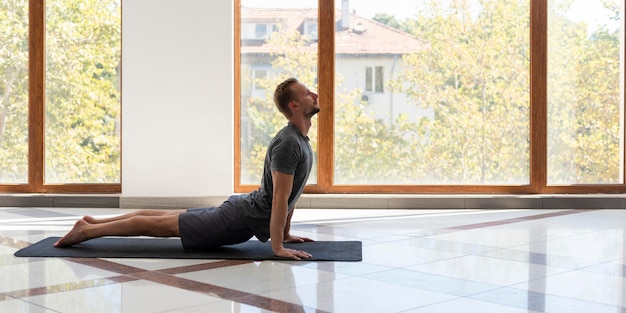 Hombre de tiro completo haciendo perro boca arriba en estera de yoga interior