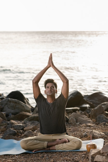 Foto gratuita hombre de tiro completo haciendo yoga en la playa