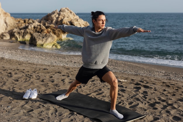 Hombre de tiro completo haciendo yoga en la playa